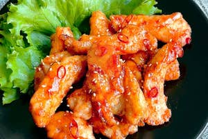 スパイシーな鶏肉料理がレタスと共に黒い皿に盛り付けられている。赤唐辛子がトッピング。