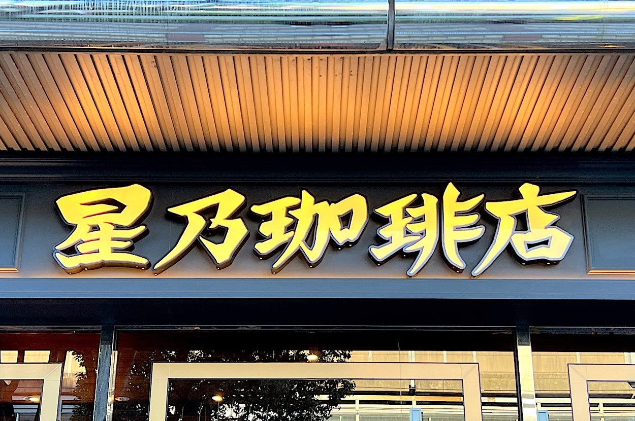 Shopfront sign with large gold letters in Chinese, reflecting trees from glass windows below, combining traditional and modern aesthetics