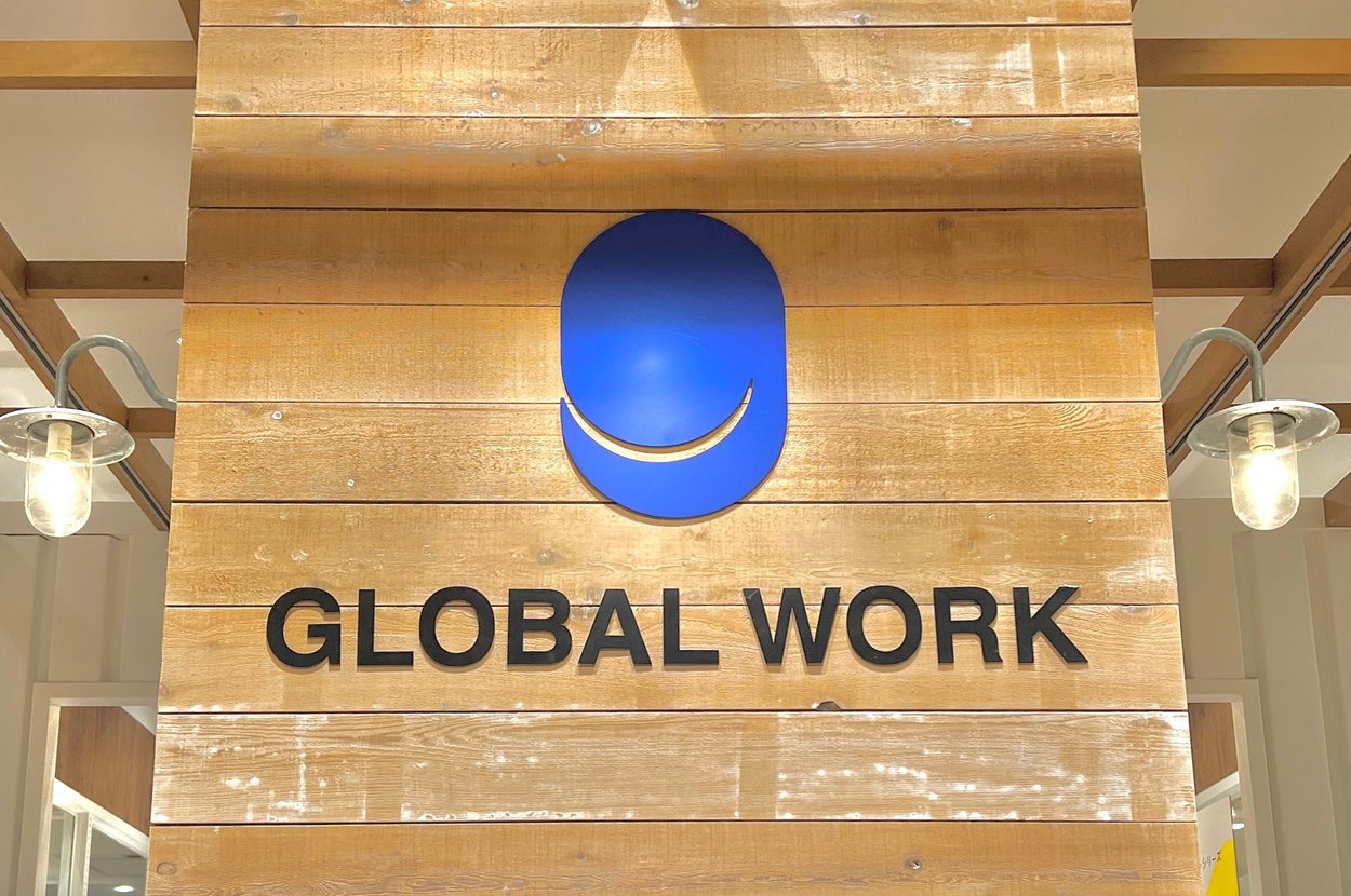 木製の背景に「GLOBAL WORK」と書かれた看板があり、上部に青い丸いロゴが配置されています。