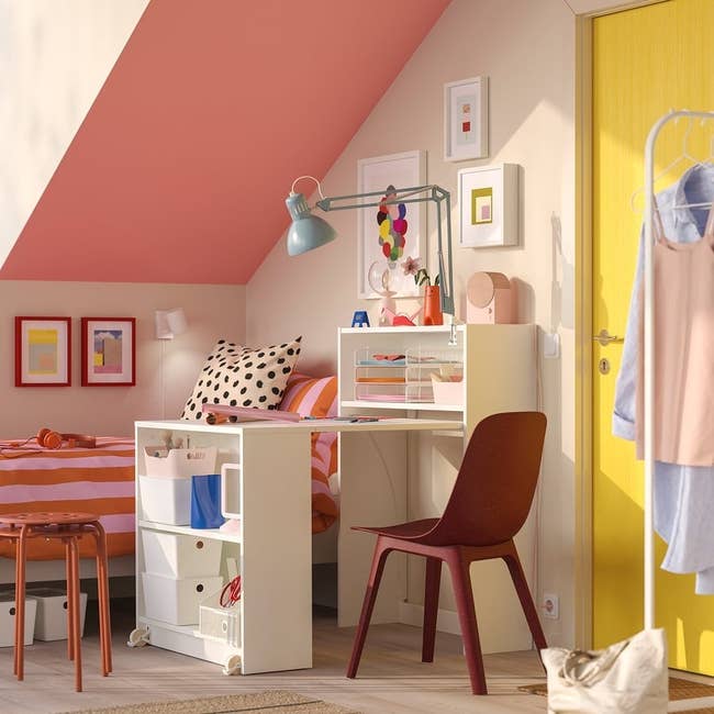 Stylish kids' country with a desk, reddish chair, and colorful decor. Organized shelves and playful patterns make a vibrant, cozy atmosphere