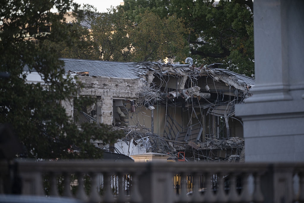 Building structure with significant damage, exposing interior rooms. Debris and steel beams are visible among partially collapsed walls
