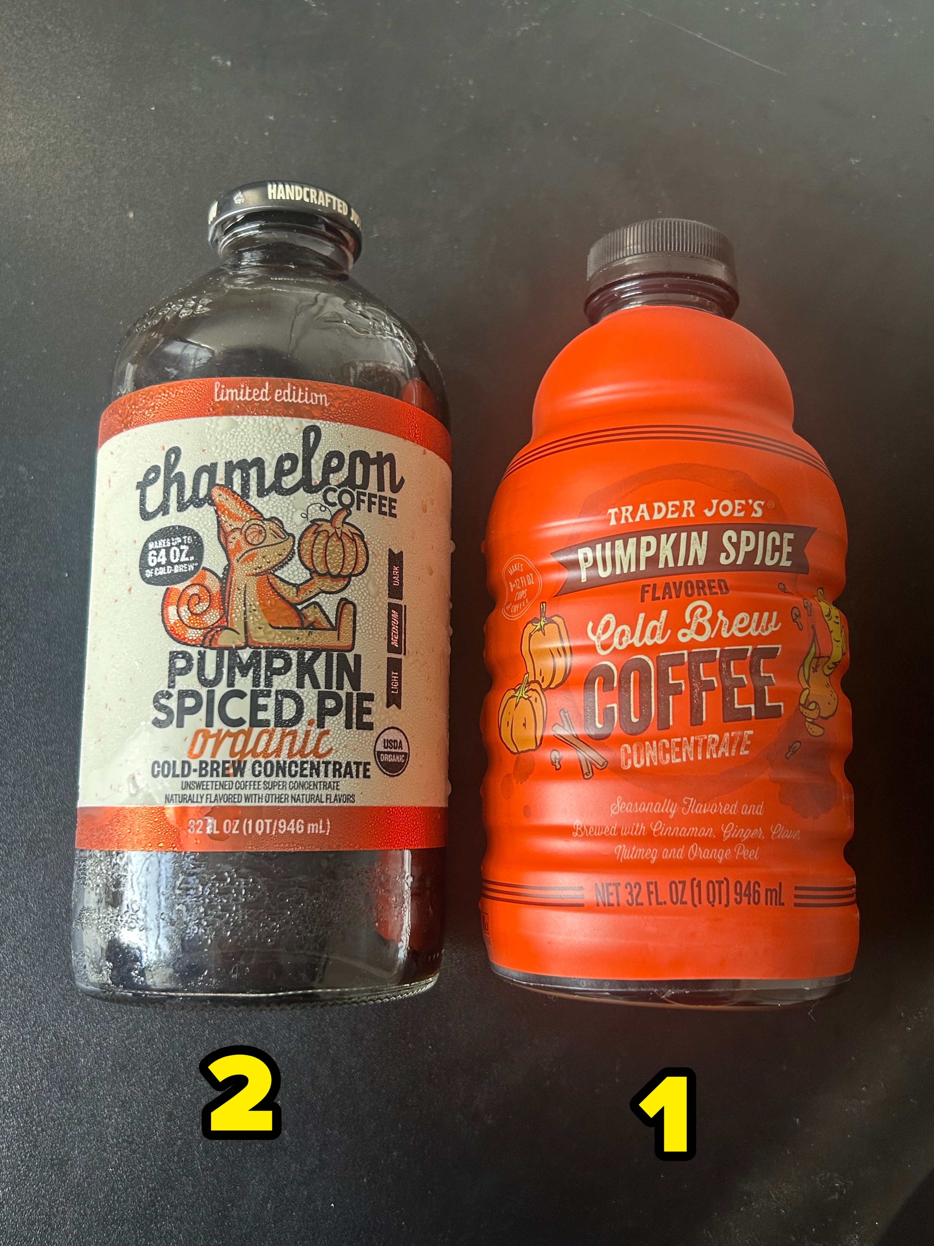 Two bottles of pumpkin spice cold brew coffee concentrate from different brands, Chameleon and Trader Joe&#x27;s, on a dark surface