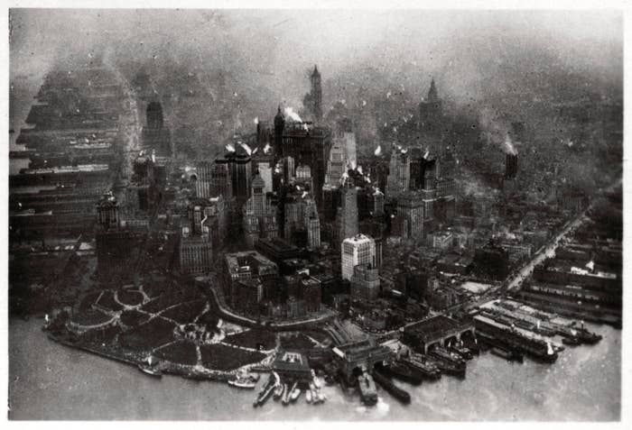 Aerial view of a smoke-filled, early 20th-century urban skyline with skyscrapers, docks, and a waterfront