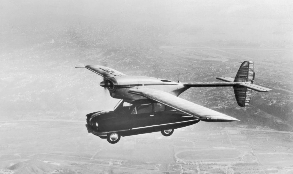 Vintage flying car prototype with wings attached to a car body, flying over landscape