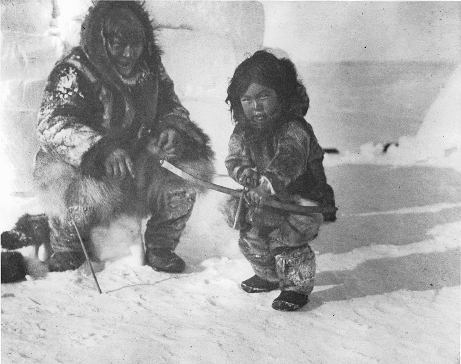 Two Inuit individuals in traditional fur garments sitting and standing on snow, one holding a bow