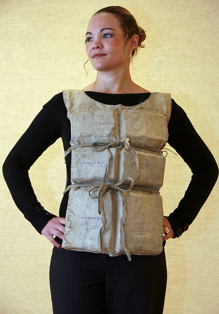 A person wears a historical style life vest with ropes tied in front, standing confidently with hands on hips