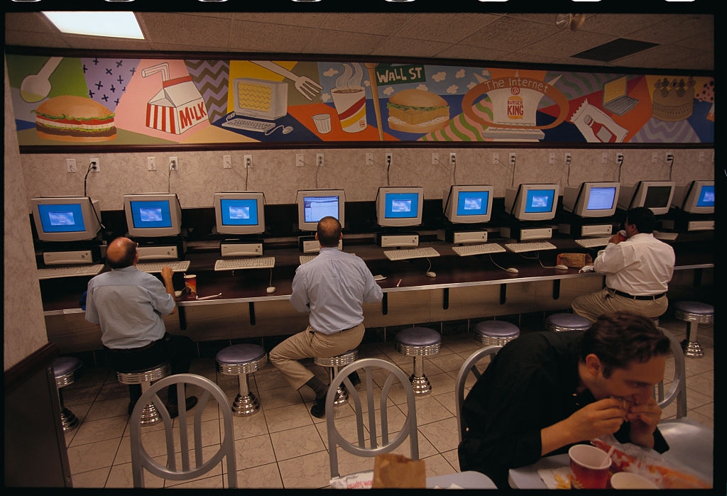 People seated at computer stations in a fast food restaurant with a mural depicting various foods and Wall Street