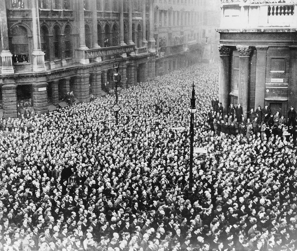 Large crowd gathers outside a historic bank building in an early 20th-century urban scene
