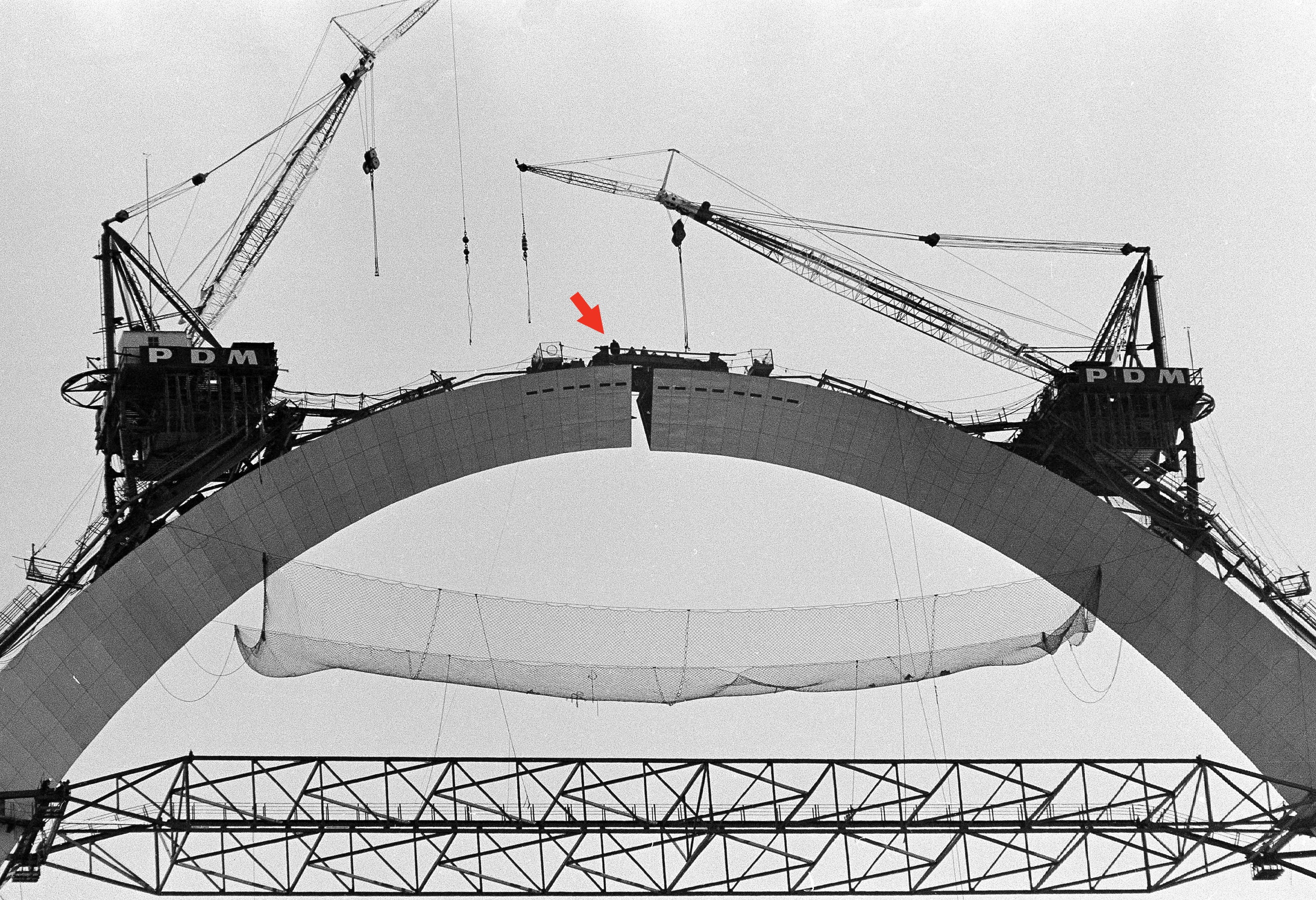Construction workers and cranes on top of the Gateway Arch during its assembly, with partial framework visible