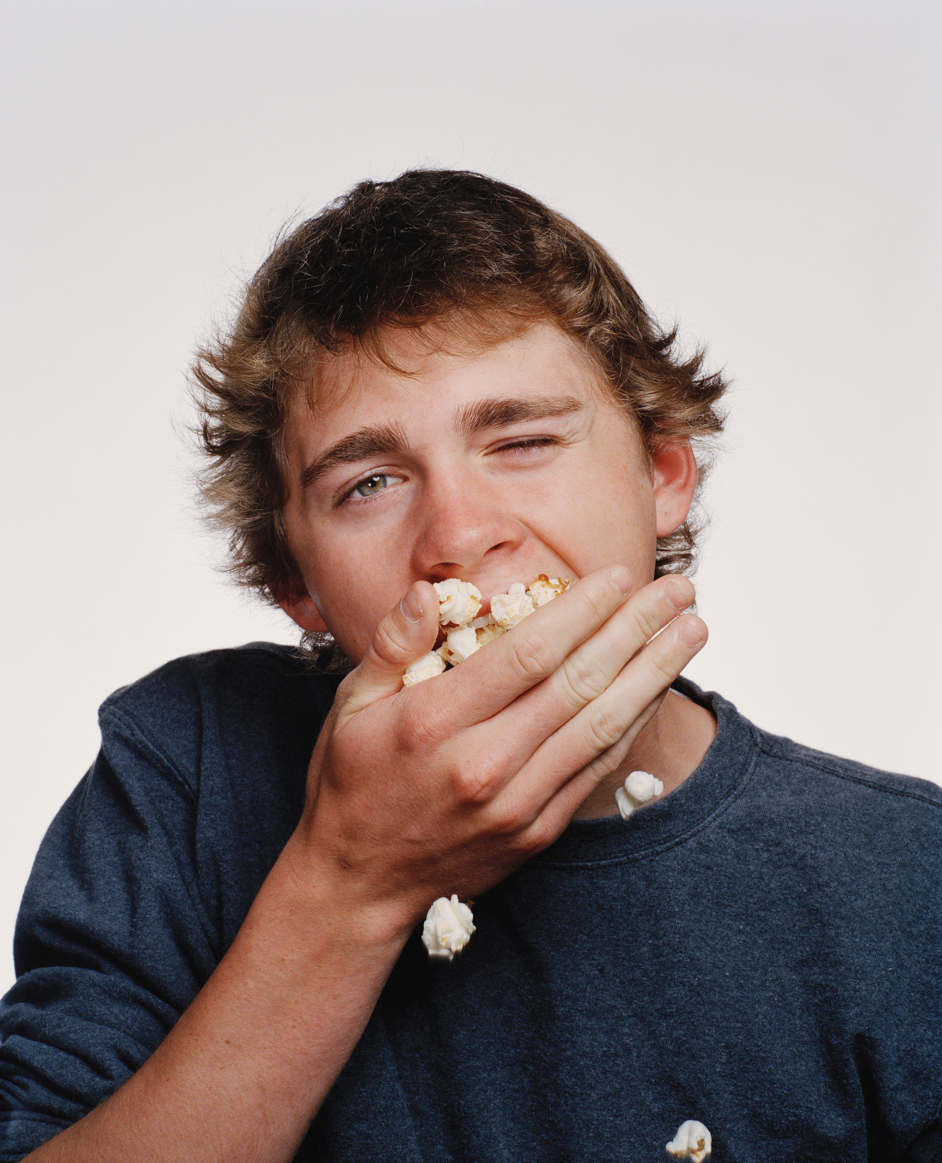 Person i en uformell skjorte som lekende spiser popcorn, holder det til munnen med én hånd, med et morsomt uttrykk