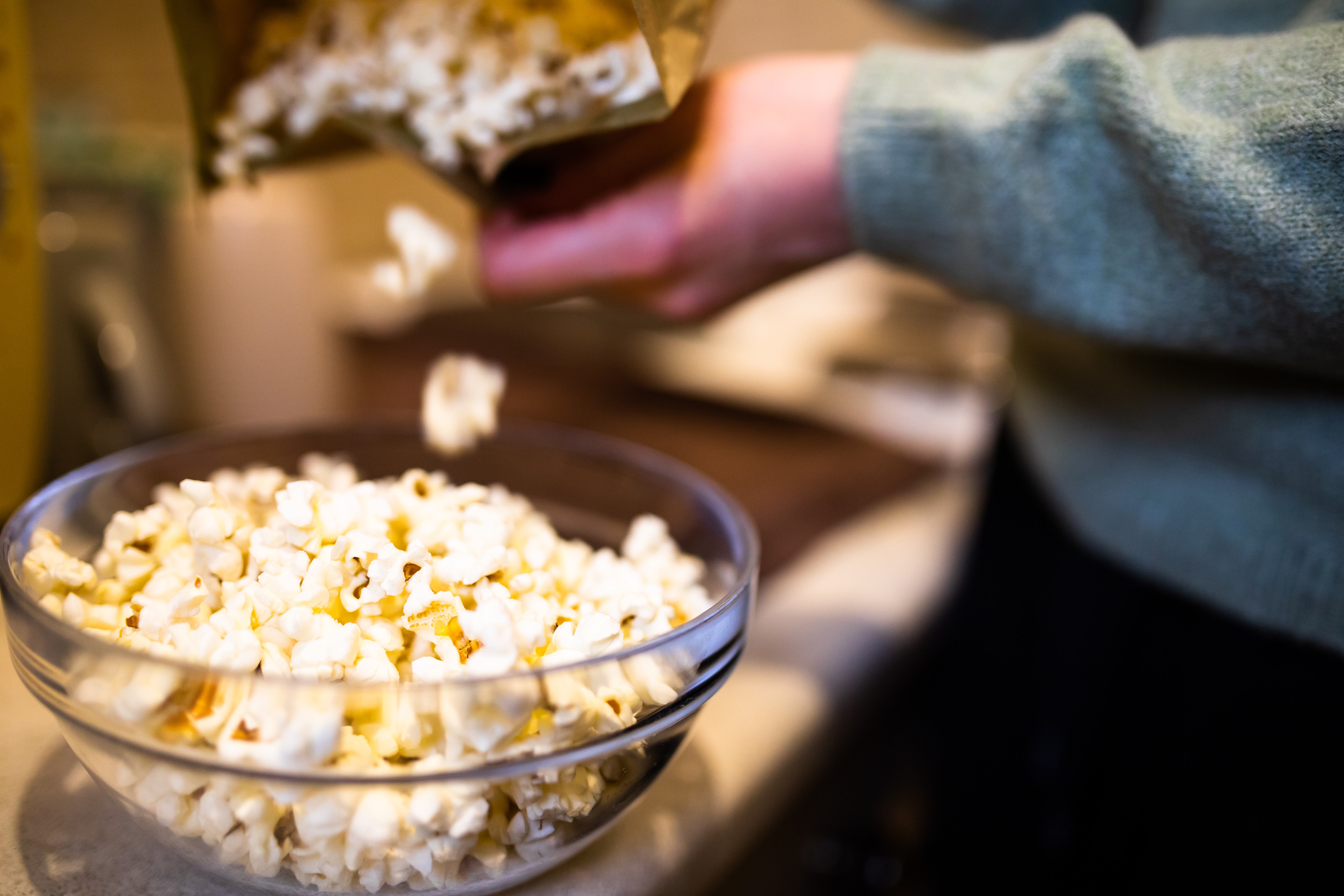 Popcorn helles fra en pose i en klar glassbolle på en benke
