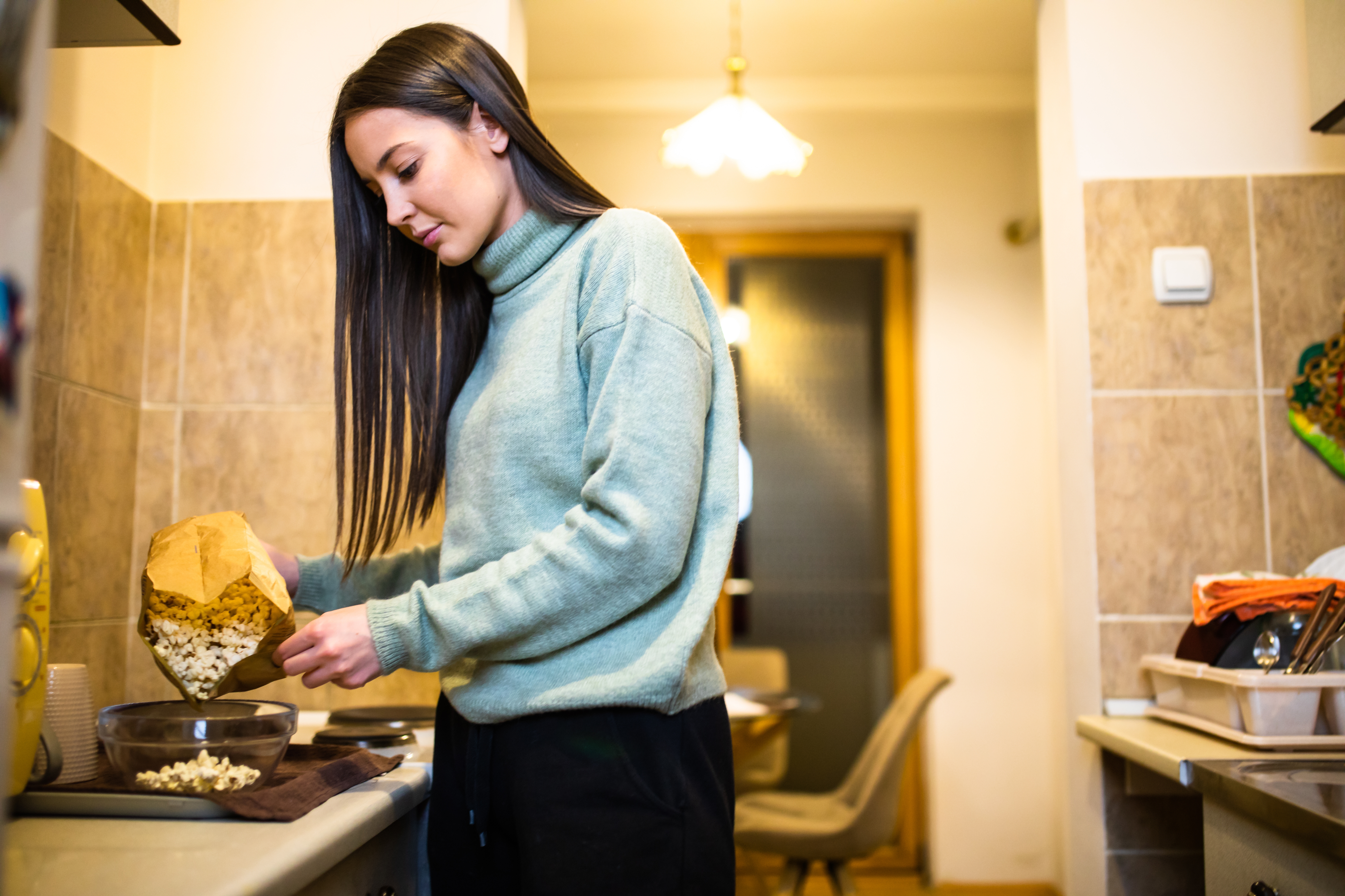 En person lager popcorn på et kjøkken og heller det fra en pose i en bolle