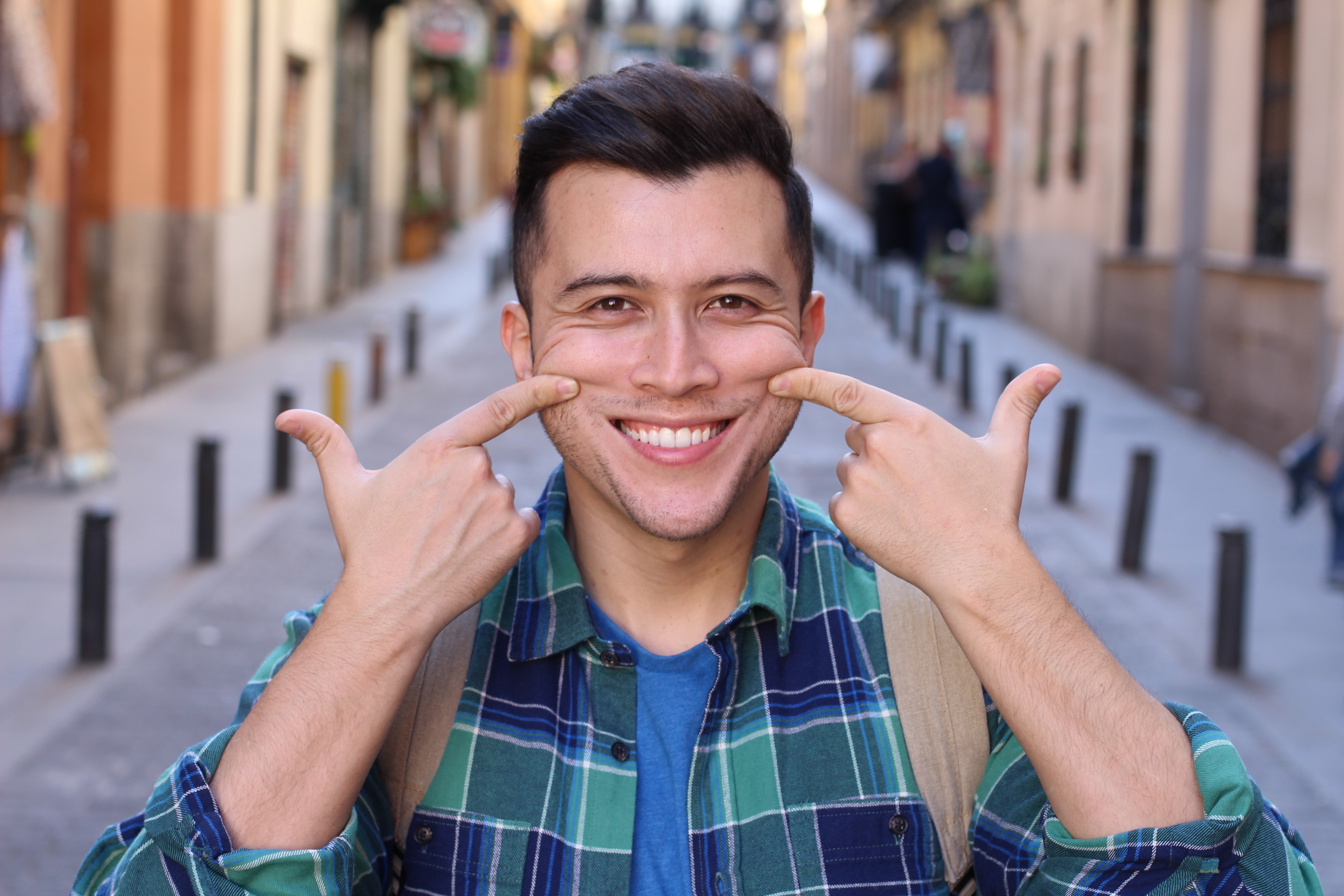 A idiosyncratic   smiling broadly, pointing astatine  their cheeks with some  scale  fingers, lasting  connected  a metropolis  street