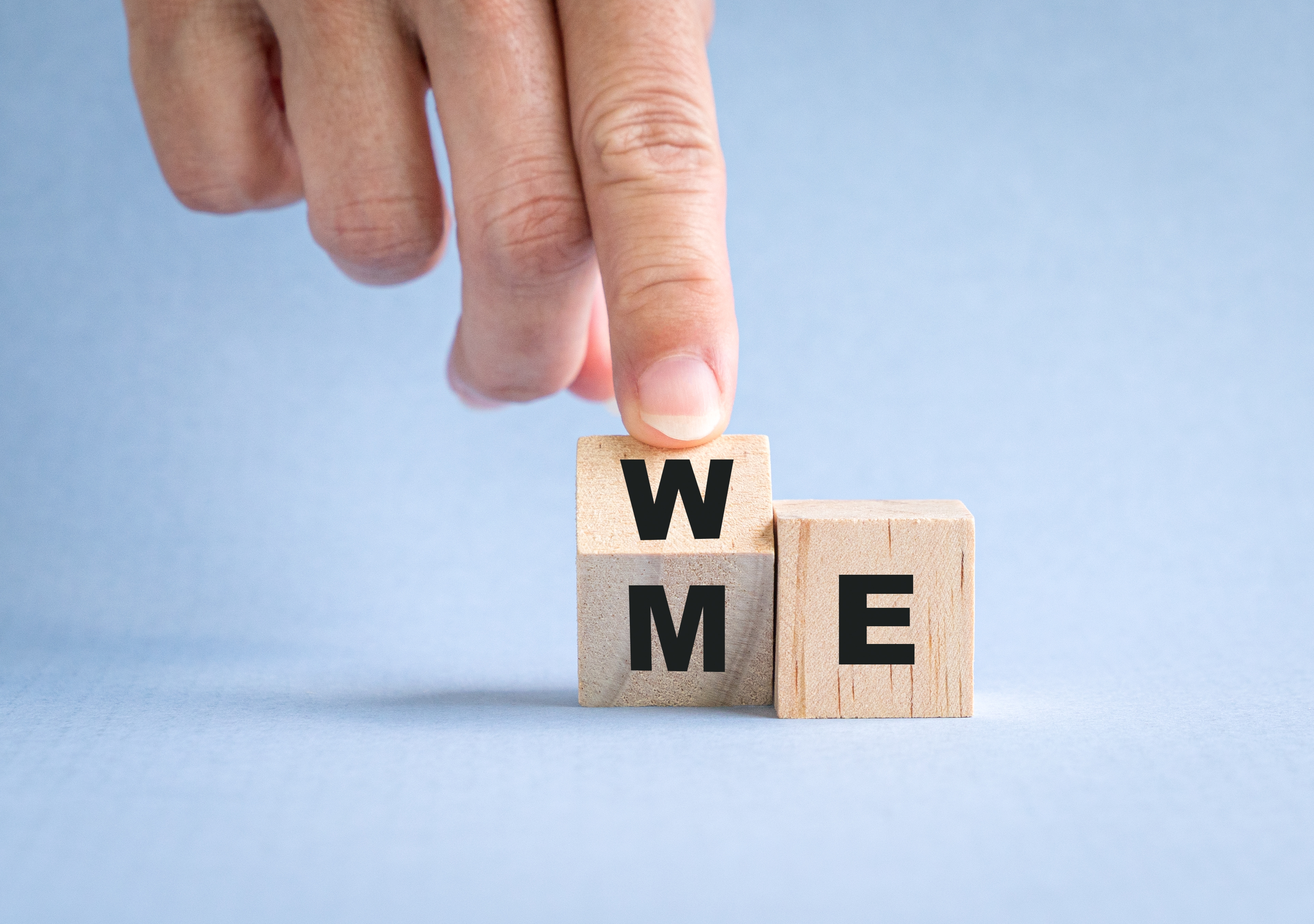 Hand stacking missive  blocks to spell &quot;ME,&quot; changing from &quot;WE.&quot;