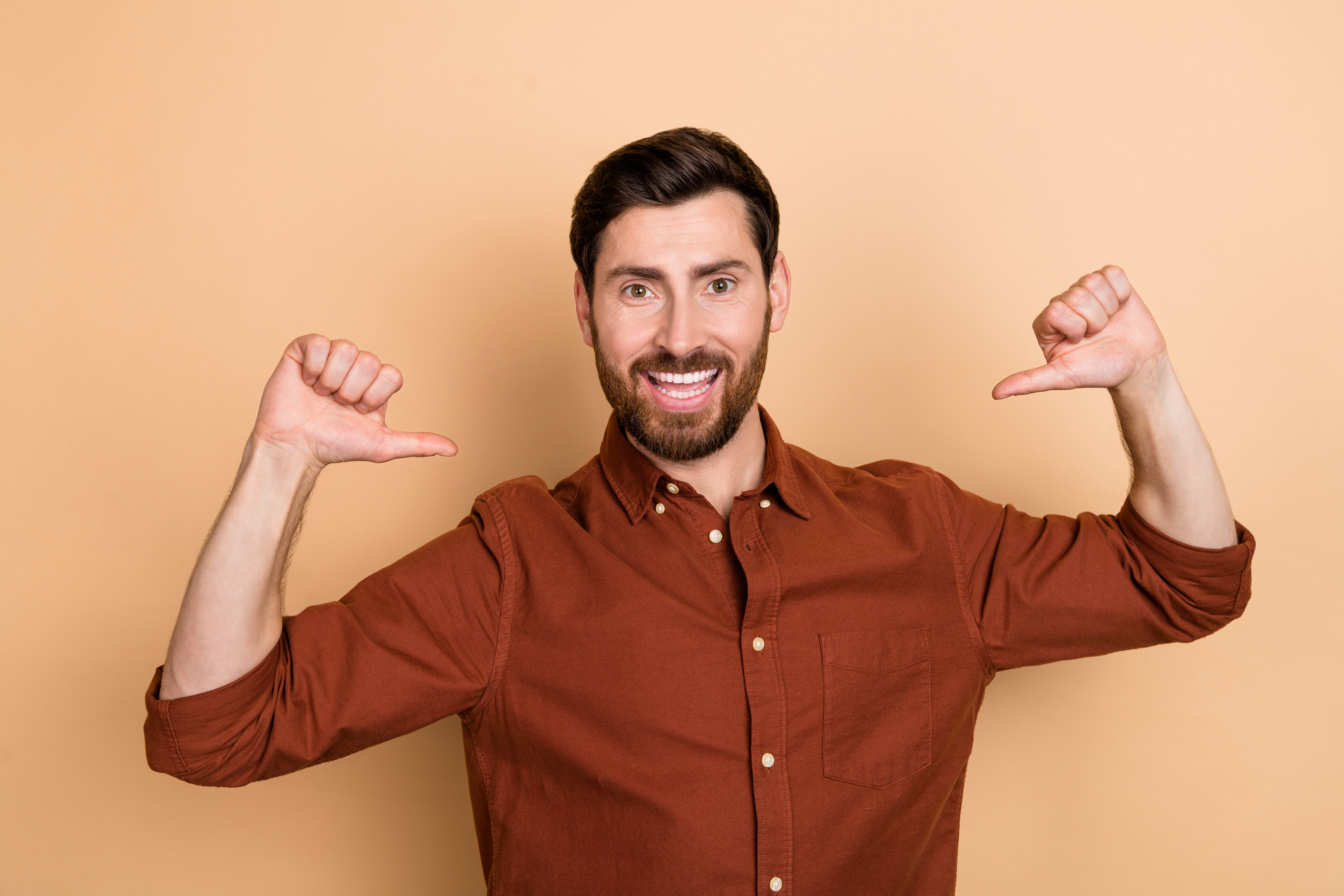 Man smiling and pointing to himself with some  thumbs up   against a plain background