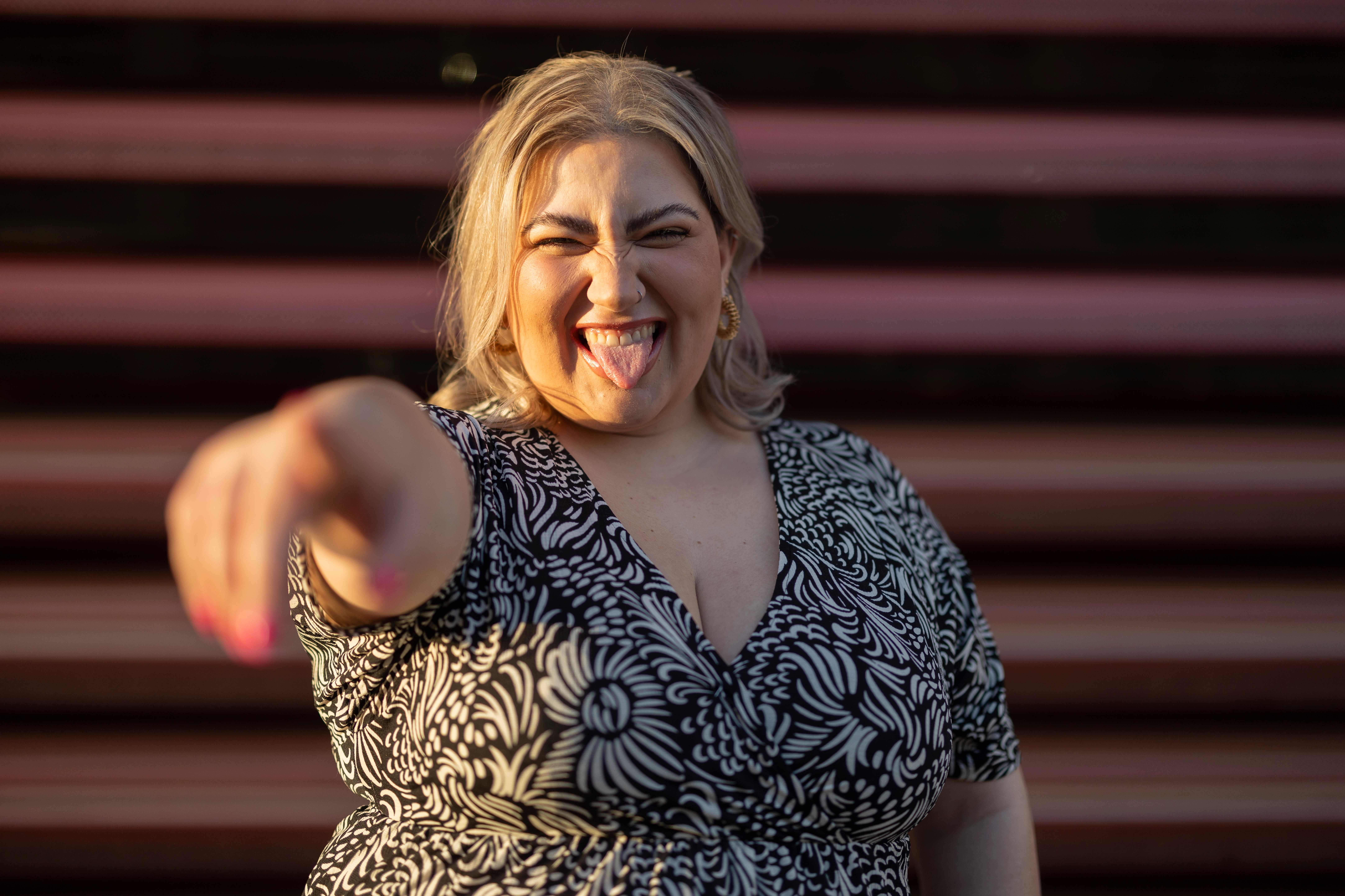 Person playfully sticking retired  lingua  and pointing astatine  the camera, wearing a floral patterned dress