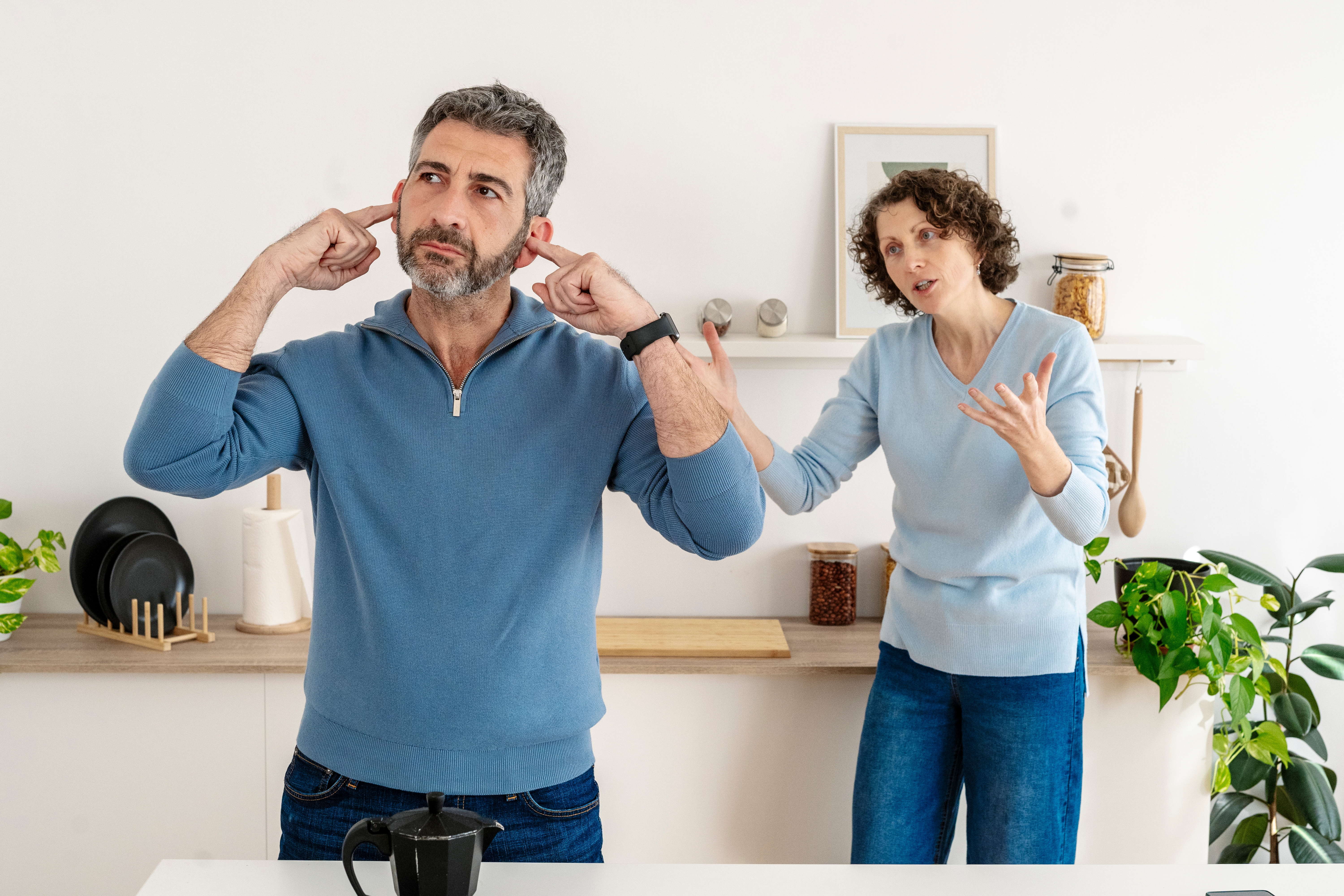 Man ignoring a pistillate   by covering his ears, portion    she appears to beryllium  speaking animatedly successful  a room  setting