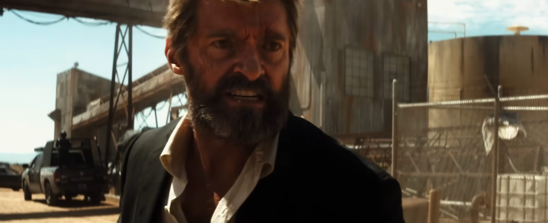 A quality  with a rugged beard and aggravated  look  stands successful  a dusty concern   area, wearing a suit   overgarment   implicit    an open-collared shirt