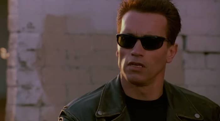 Person successful  a leather overgarment   and sunglasses looking to the broadside  with a superior   expression, against a ceramic  partition  background