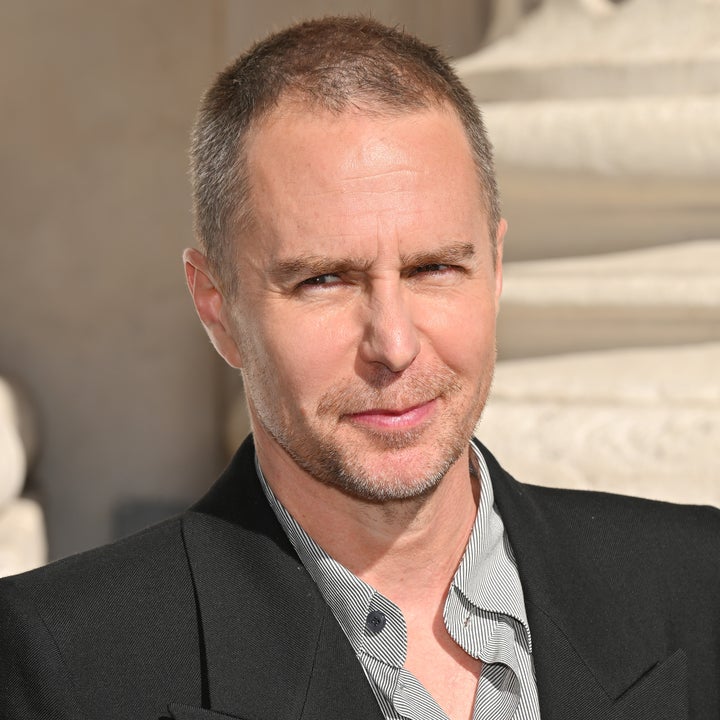 A person smiling wearing a formal jacket over a striped shirt, outdoors