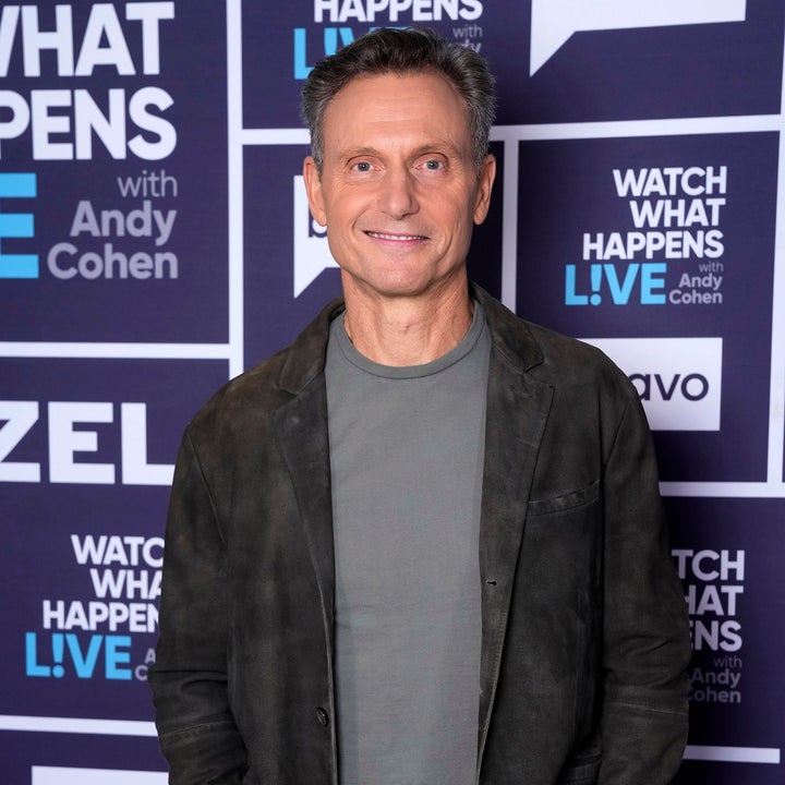 Man in casual jacket and t-shirt poses at "Watch What Happens Live" event with branded background