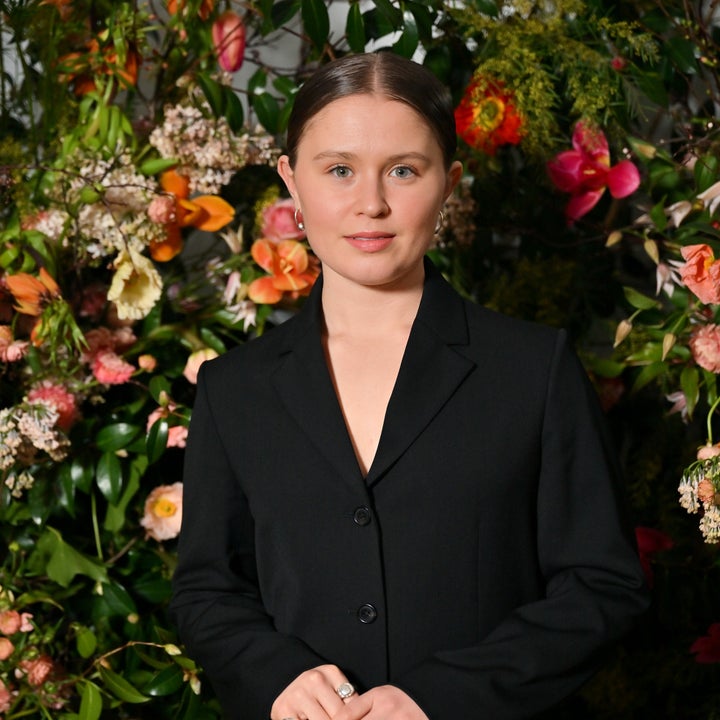 Person in a black suit stands in front of a vibrant floral backdrop