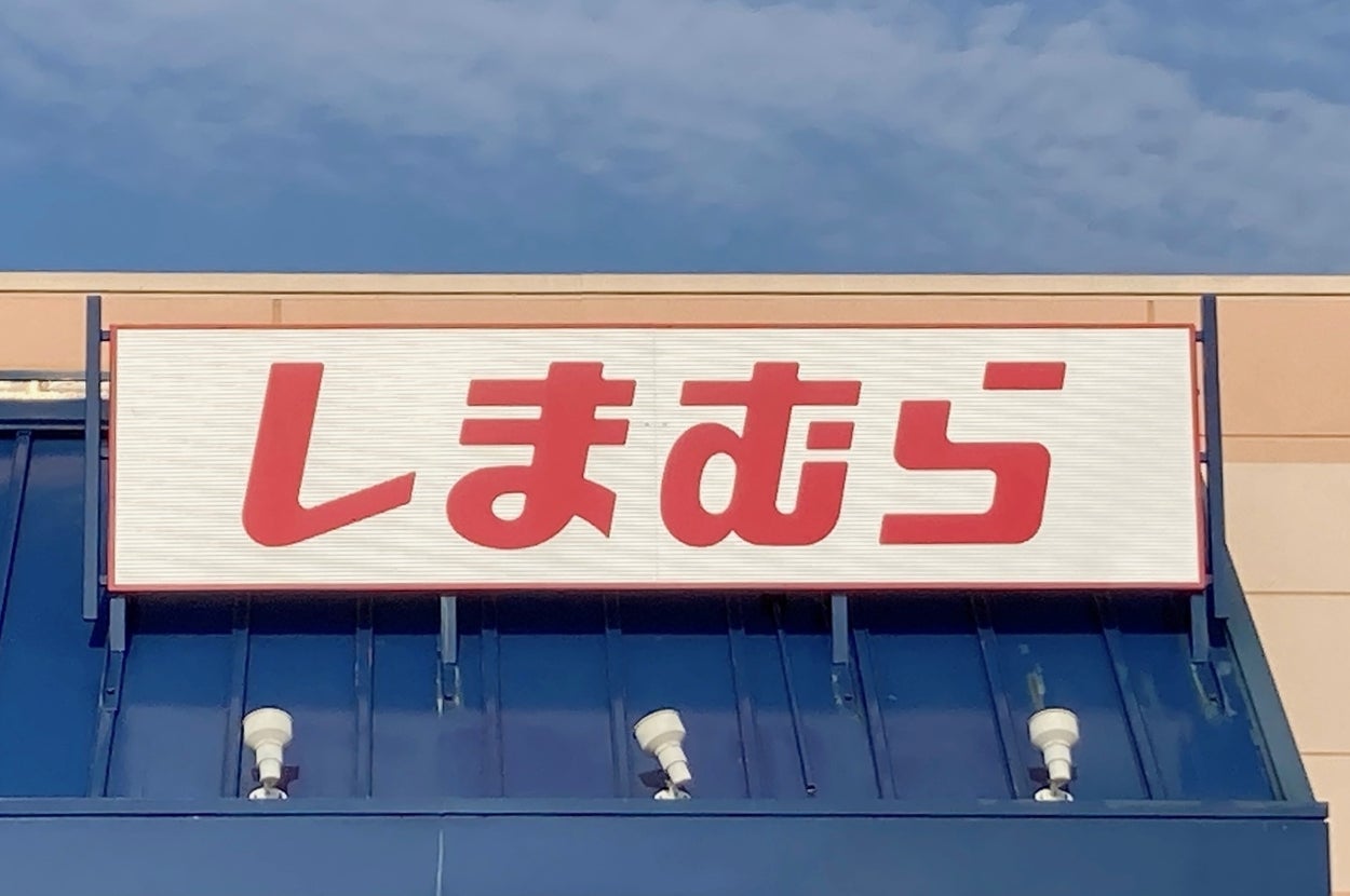 The image shows a storefront sign with Japanese text reading "しまむら" above a blue awning