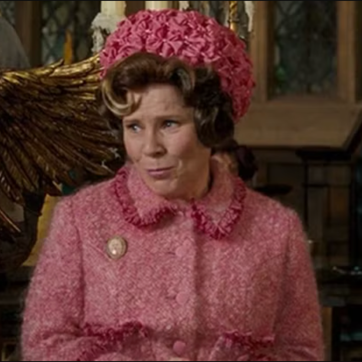 A character in a pink, vintage-style outfit stands by a golden eagle podium in an ornate room
