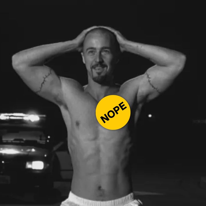 A shirtless man stands with hands on head, displaying tattoos. Police car in background