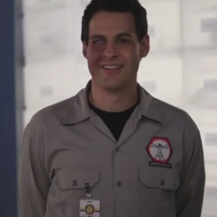 Person in a uniform-style shirt with a logo, standing indoors, smiling at the camera