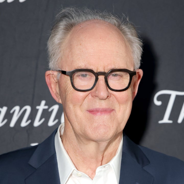 A person in a suit with glasses smiles slightly at a formal event