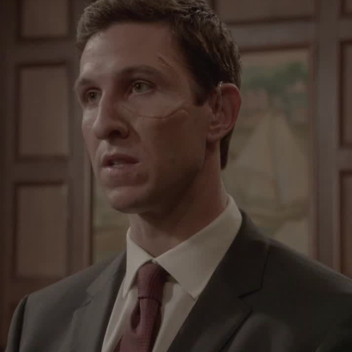 Man in a courtroom setting, wearing a suit and tie, with facial expression suggesting he's involved in a serious discussion or argument