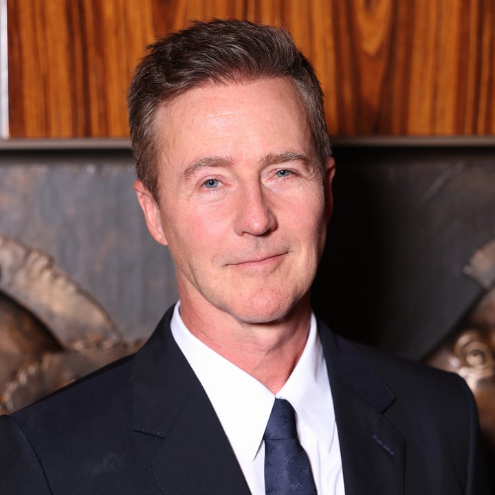 A person in a formal suit and tie at an event, posing for a photo against a wood-paneled background