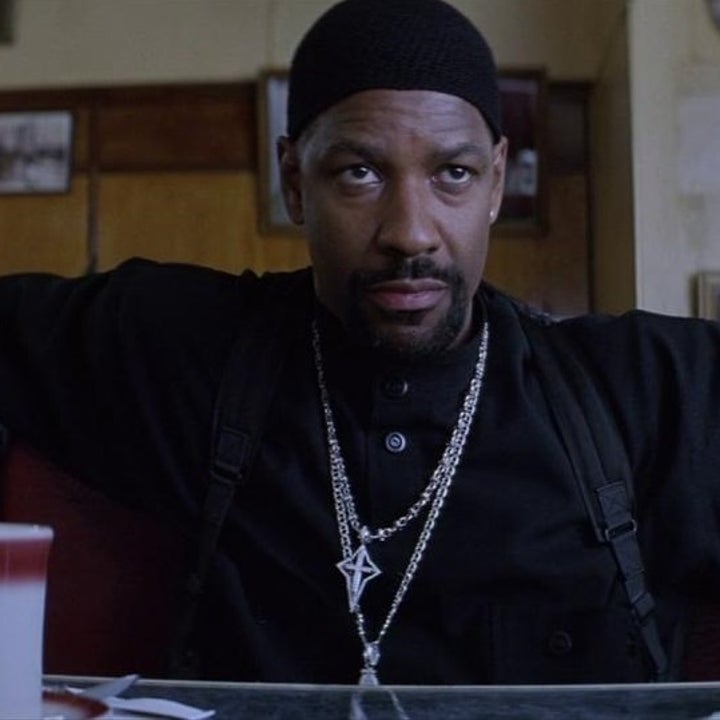 A man sits in a diner, wearing a black shirt and knit cap, with arms spread wide, looking intently forward. A cup on the table is visible