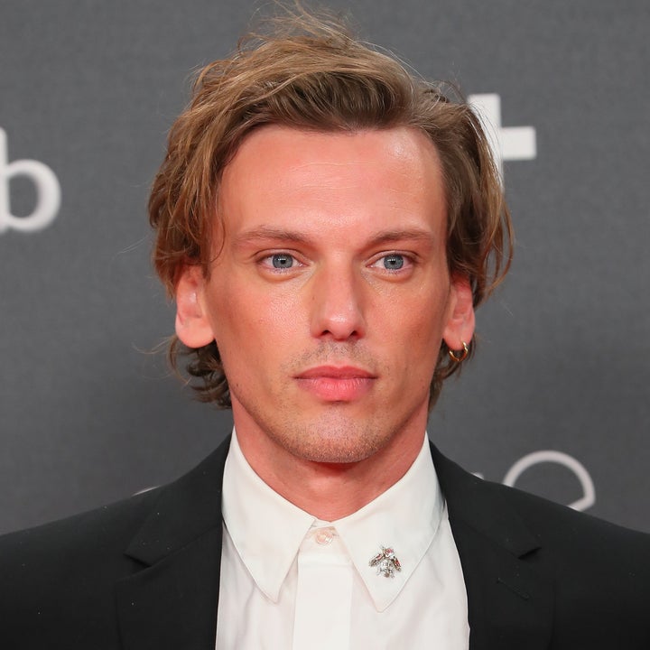 Person in a suit with an embellished shirt collar, standing against a branded backdrop