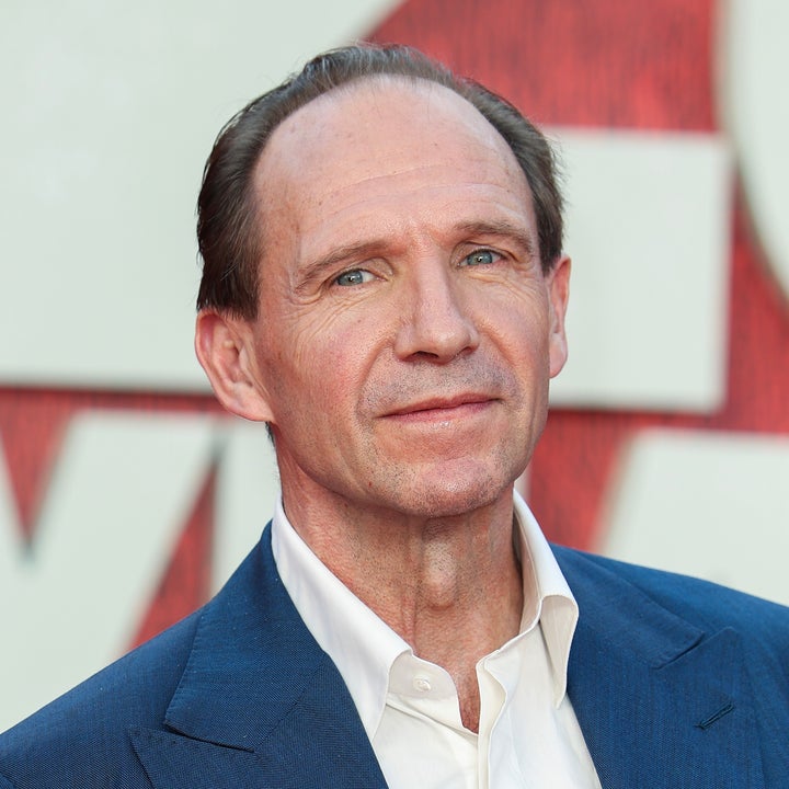 Person in a tailored suit with a white shirt, attending an event in front of a backdrop