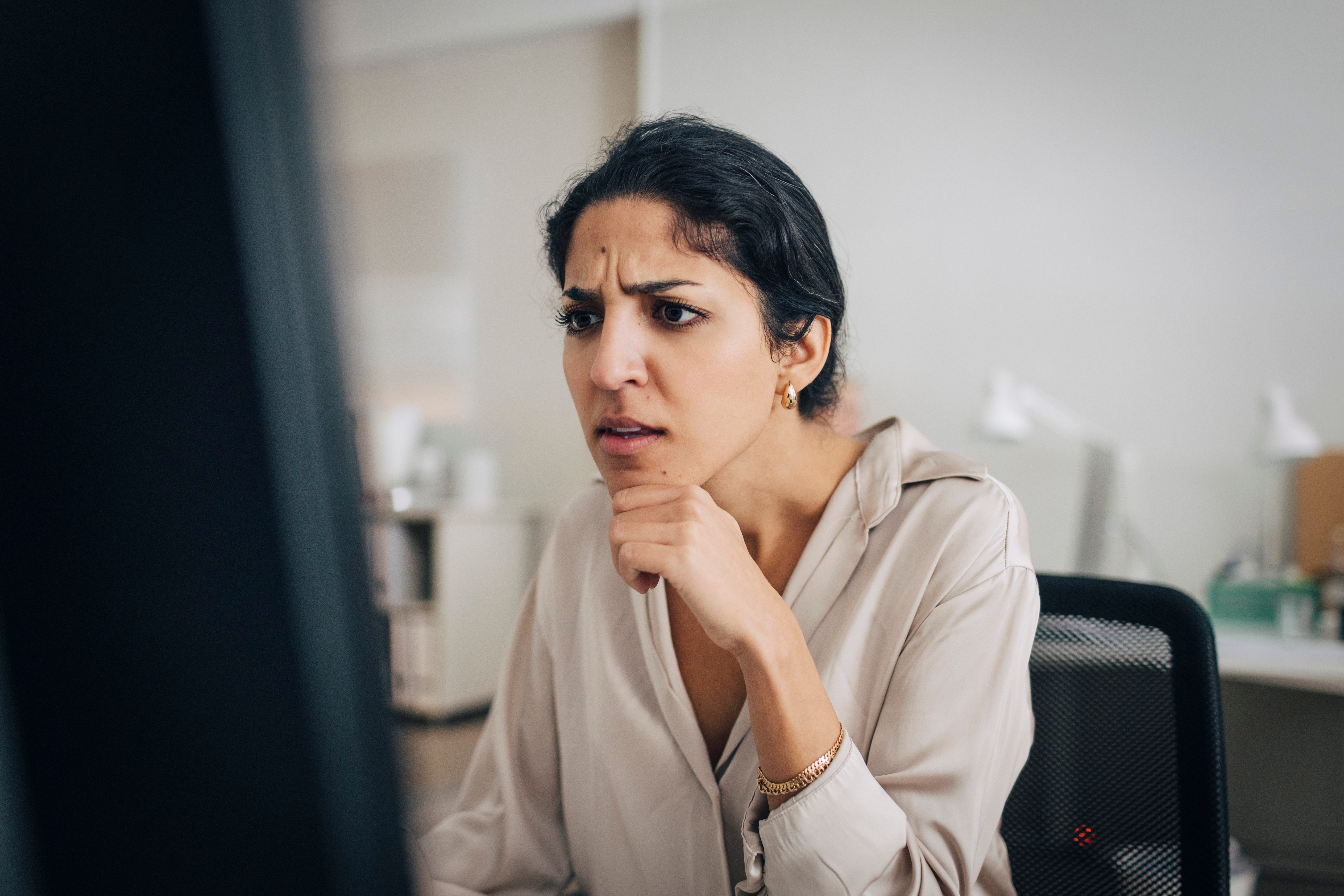 Person successful  an bureau   looking astatine  a machine  surface  with a thoughtful, puzzled expression, wearing a airy  blouse