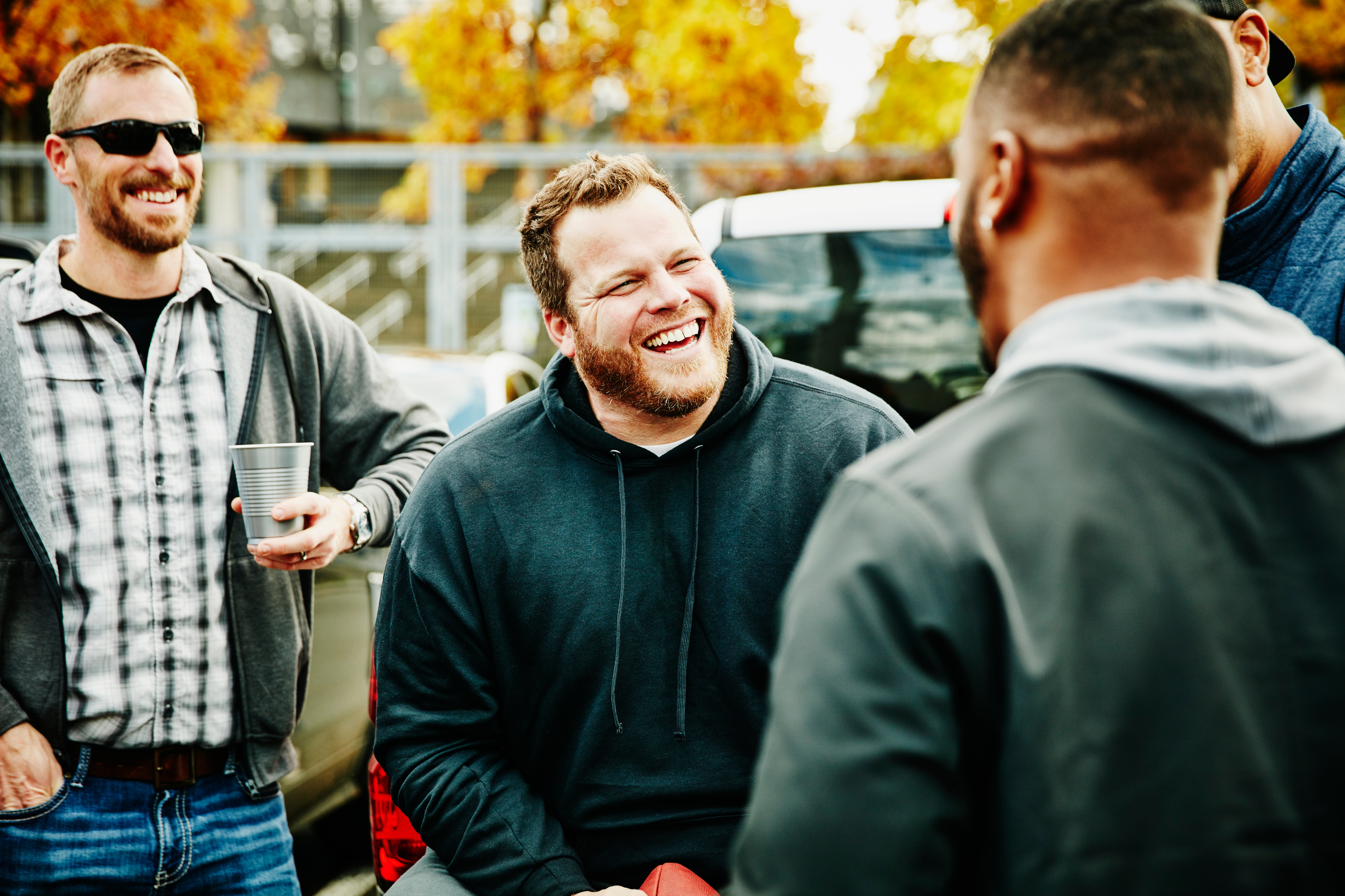 Group of radical   smiling and chatting outdoors, 1  idiosyncratic   holds a cup. Casual, affable  gathering