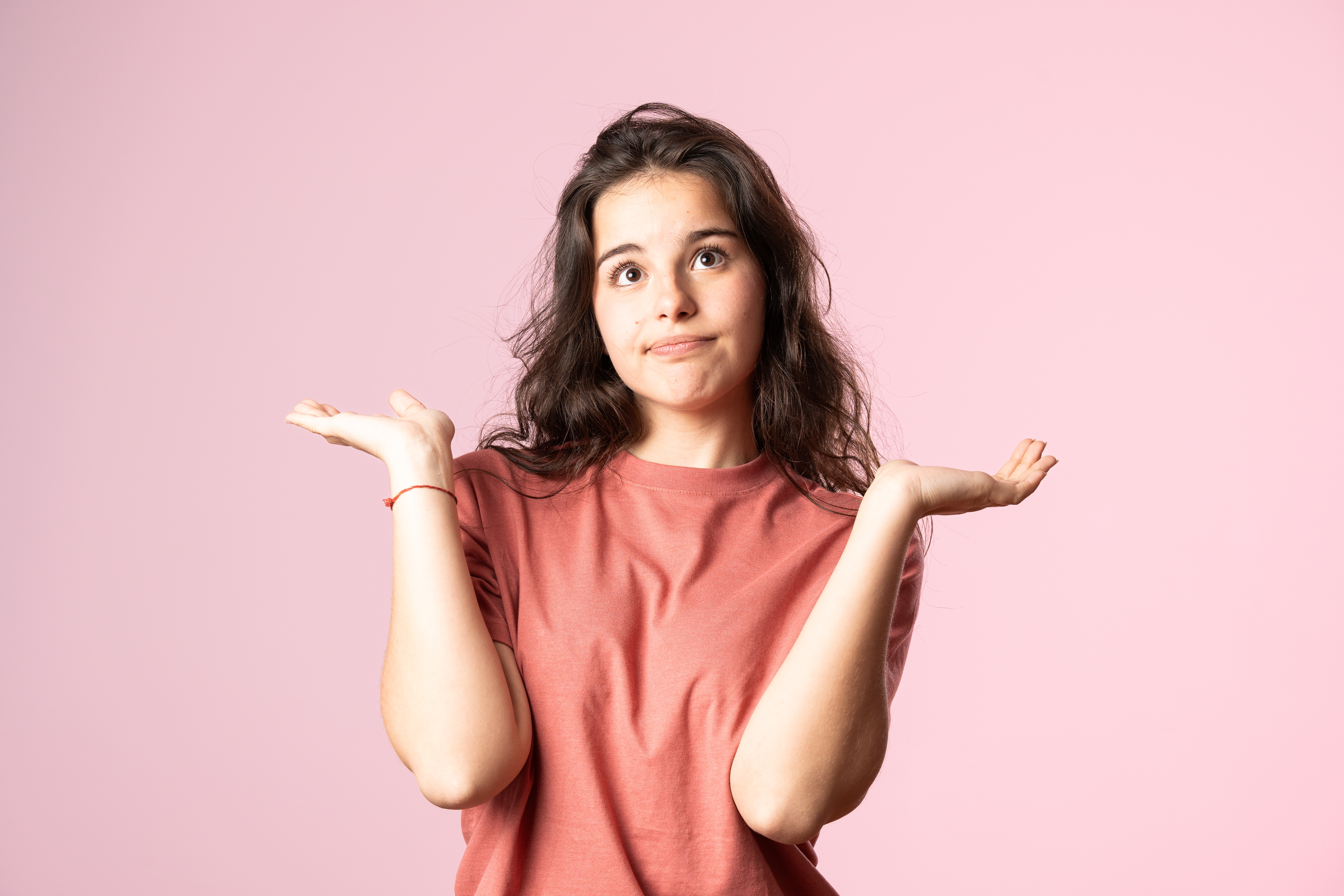 Person with agelong  hair, wearing a casual shirt, raising some  hands with a puzzled look  against a plain background