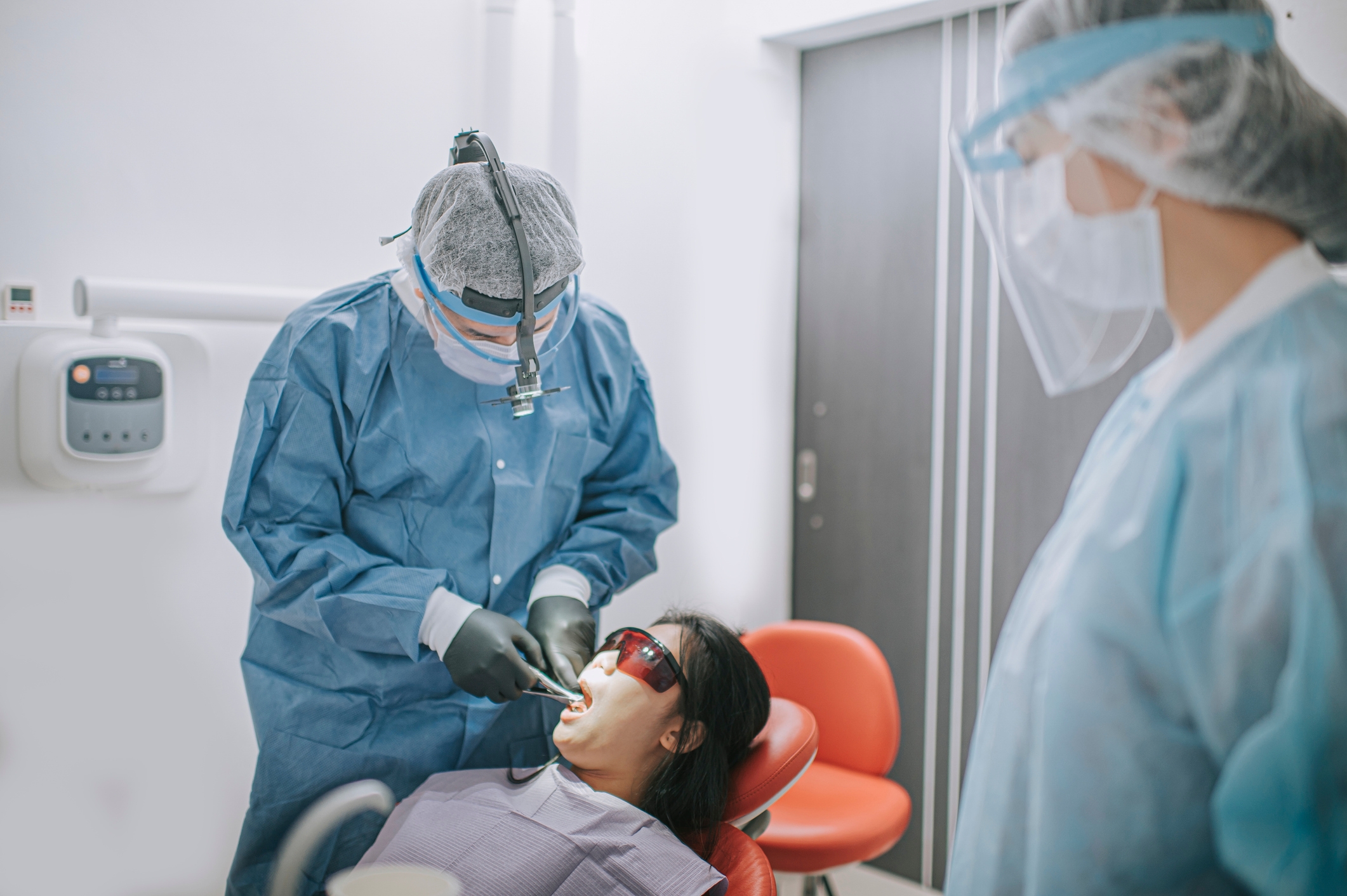 Tannlege og assistent i verneutstyr som utfører tannarbeid på pasient i en klinikk
