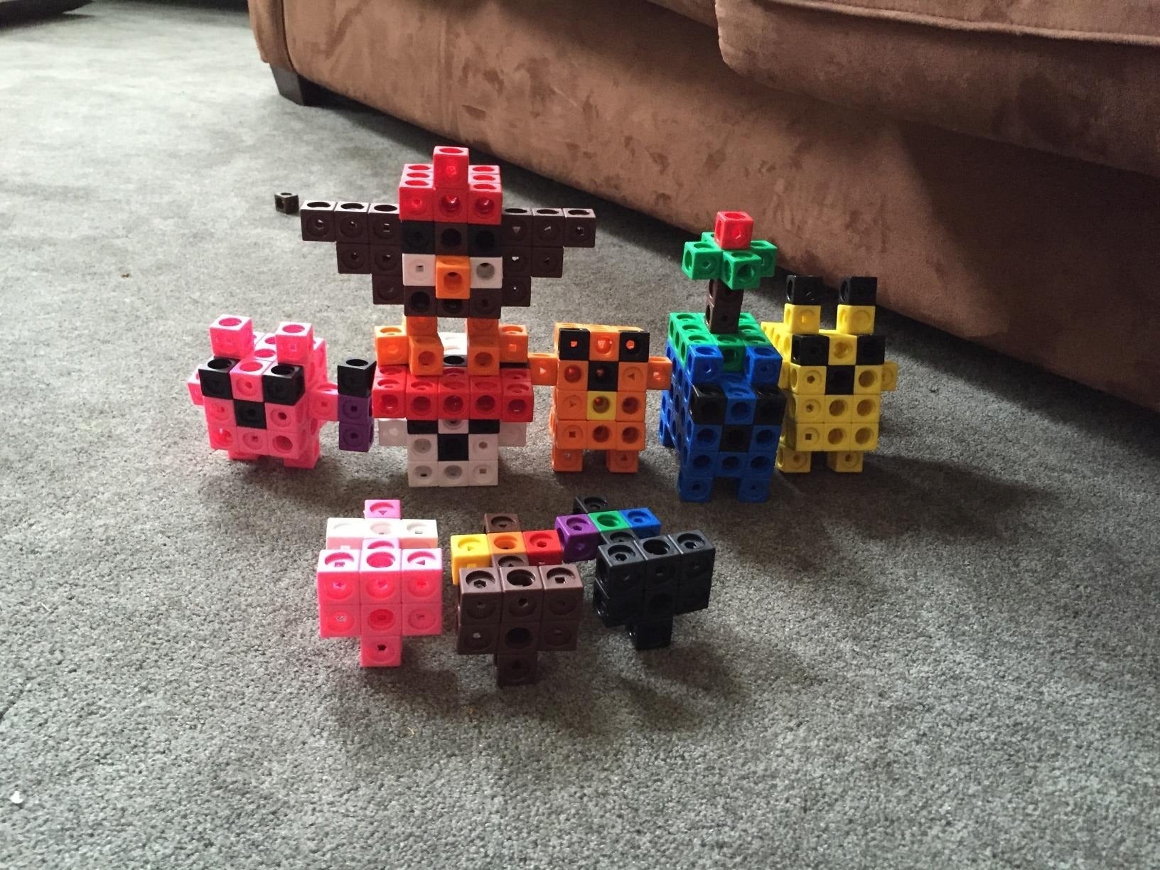 Toy artifact  figures resembling assorted  animals and objects are arranged connected  a carpeted floor