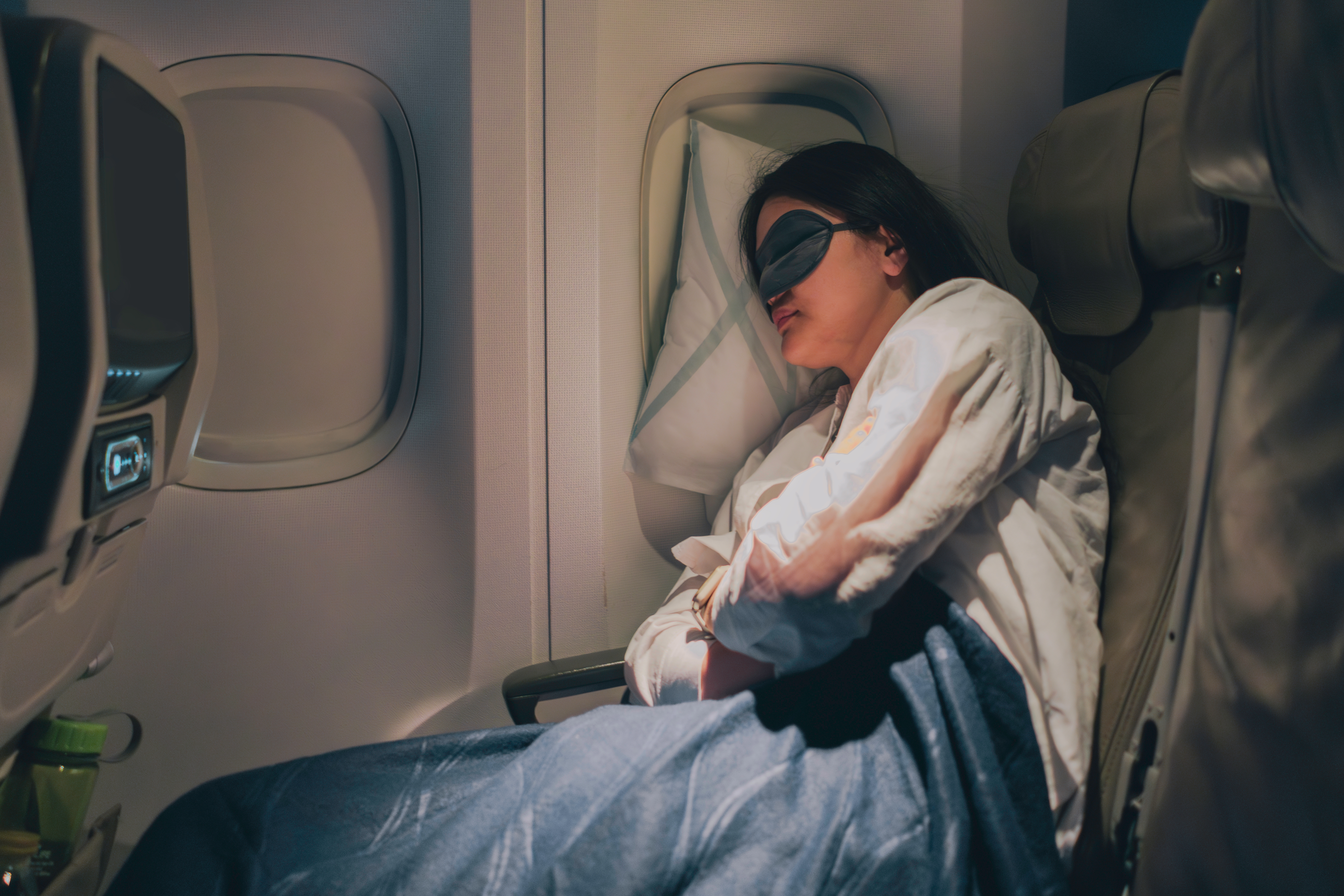 Person dormant  connected  an airplane, wearing a slumber  disguise  and blanket, leaning against the window