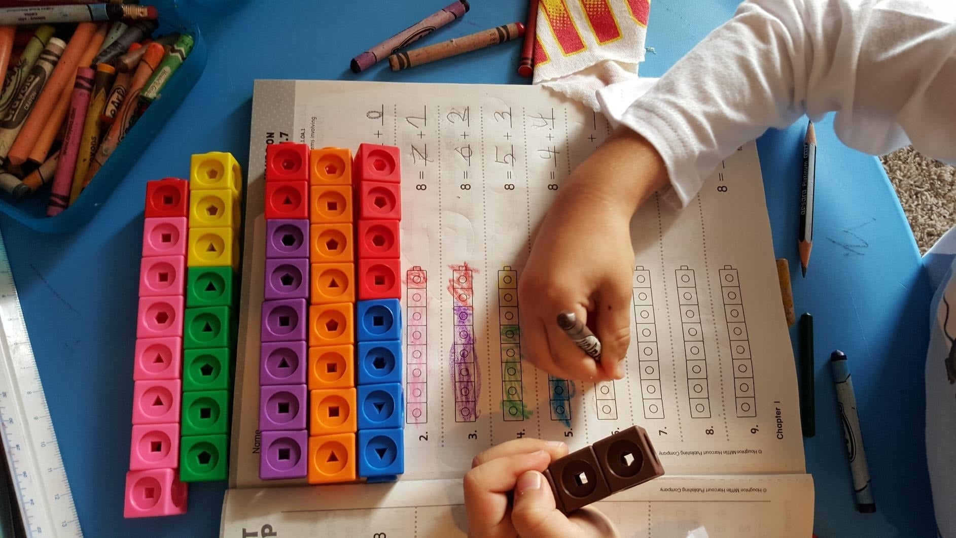 Child utilizing colorful stacking cubes to assistance  mathematics  homework, with crayons scattered connected  a desk