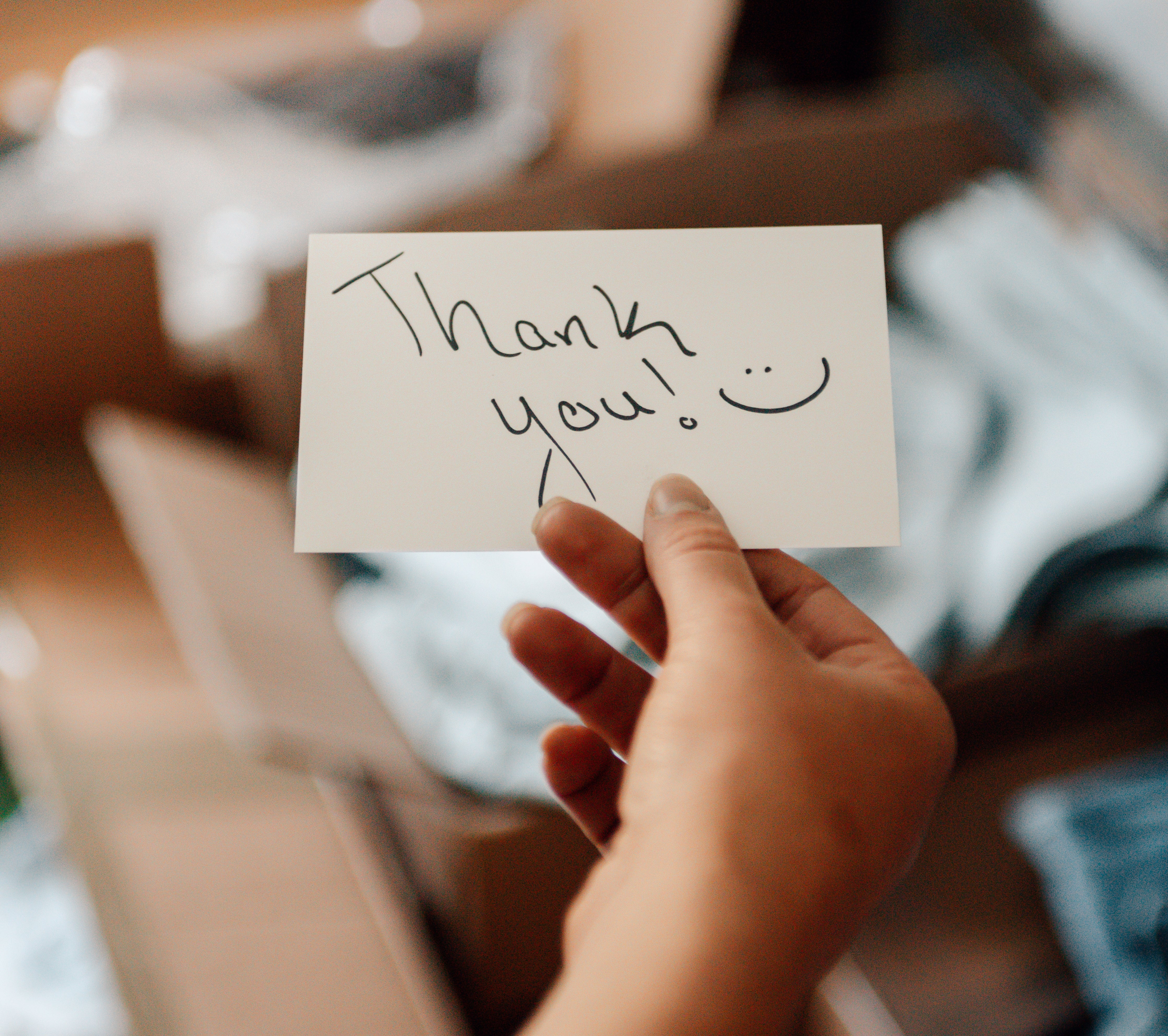 Hand holding a &quot;Thank you!&quot; enactment      with a smiley face, surrounded by unfastened  boxes