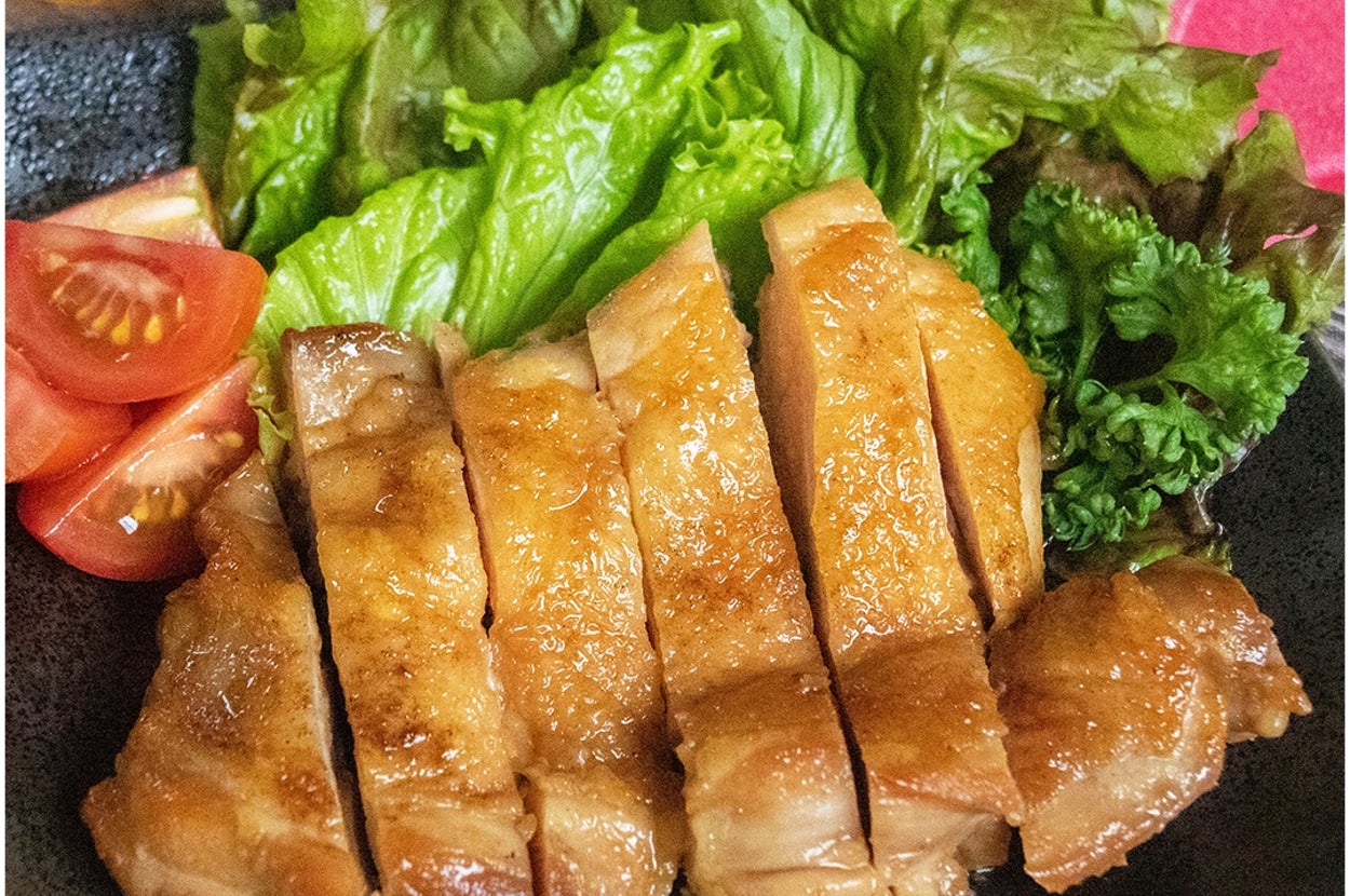 グリルチキンのスライス、レタスとミニトマトが添えられた料理の写真。