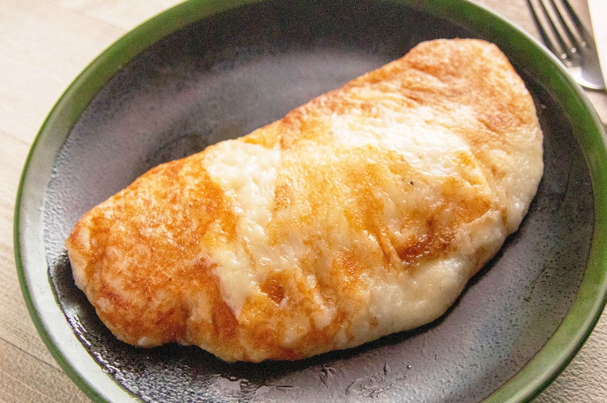 お皿に盛られた焼き色のついたオムレツ。柔らかそうな質感が美味しそうに見える。背景にフォークとナプキン。