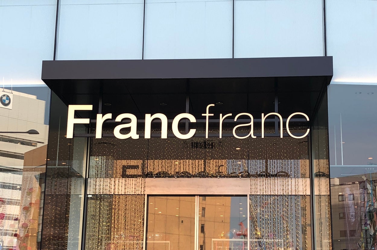 Francfrancの店舗入り口。モダンなデザインのファサードとガラス窓が特徴。都市の建物が背景に映っている。