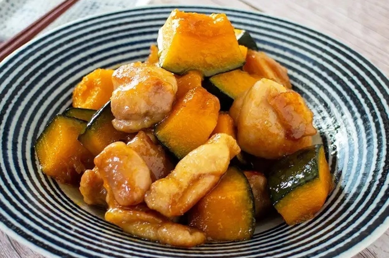 青い縞模様の皿に盛り付けられたカボチャと鶏肉の料理。背景に箸が置かれている。