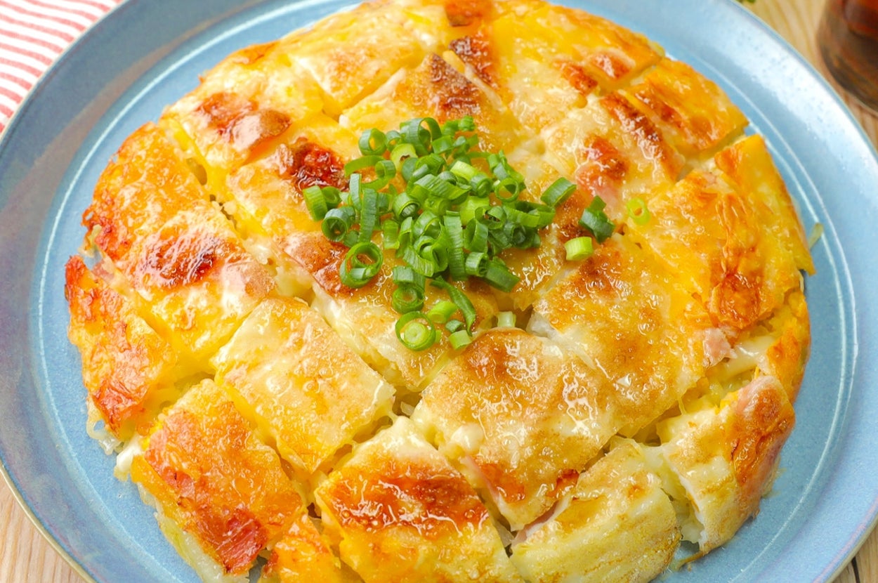 ネギがトッピングされたチーズポテトパンケーキが青い皿に乗っている。手前にストライプの布が見える。