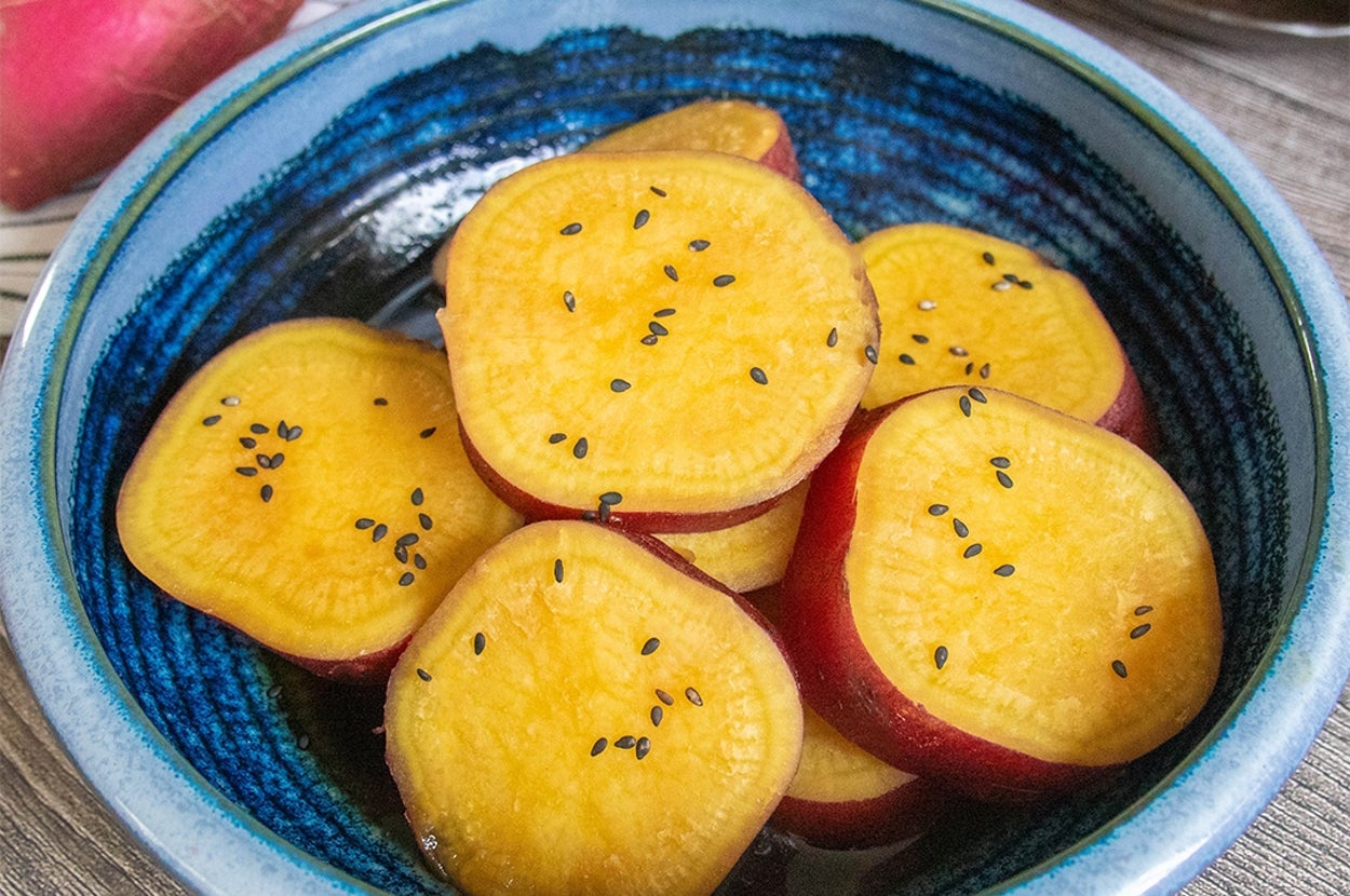 青い器に盛られた輪切りのさつまいもの煮物。黒ごまがのっている。